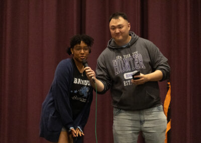 A man wearing a CUNY Hunter sweatshirt holding a microphone to a girl wearing a CUNY Baruch sweatshirt